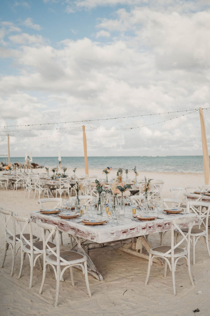 Large square wooden table on the beach set with floral arrangements