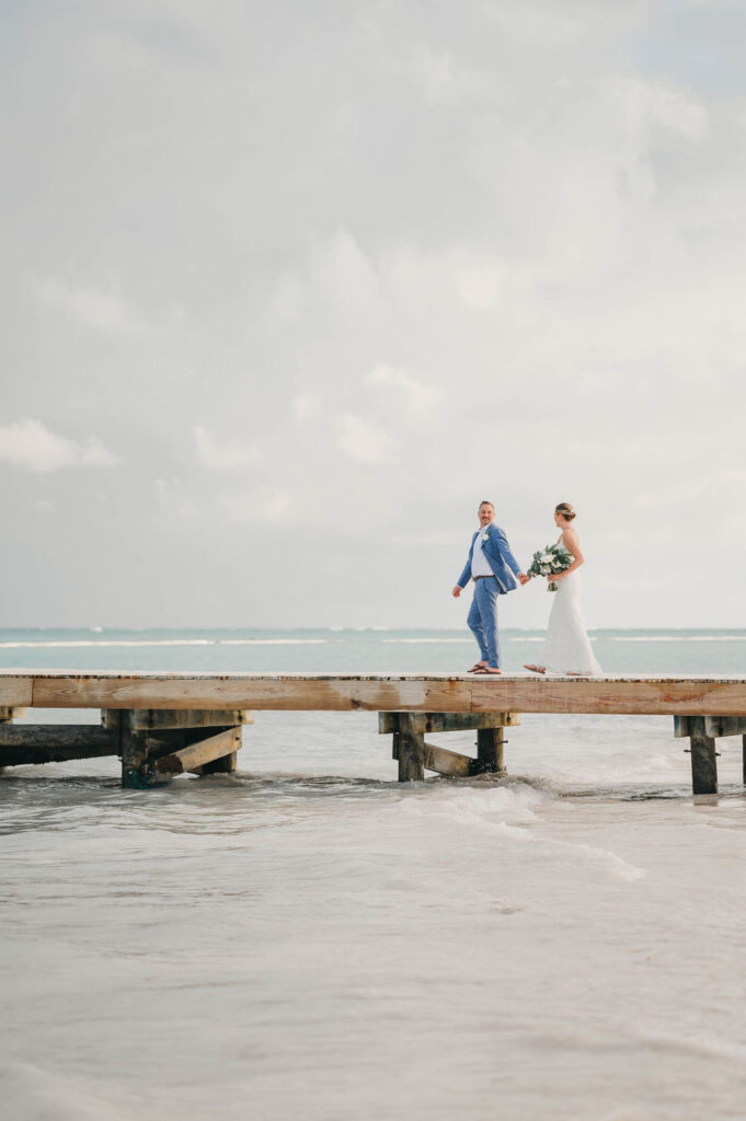 Bride and groom holding hands as they walk on a beach pier