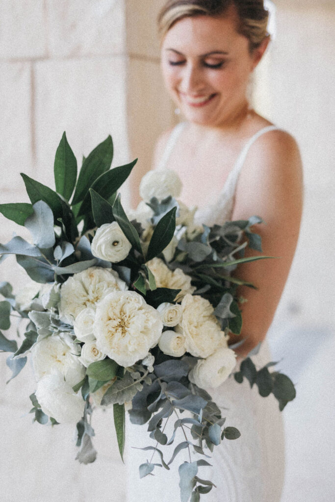 Bride in white dress holding large bouquet of white flowers, eucalyptus and greenery