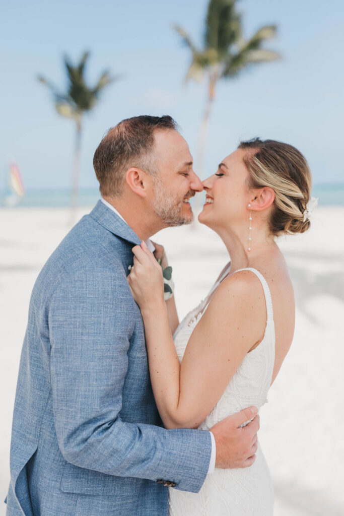 Photo of bride and groom looking happy on a beach while they hold each other close for a wedding photo