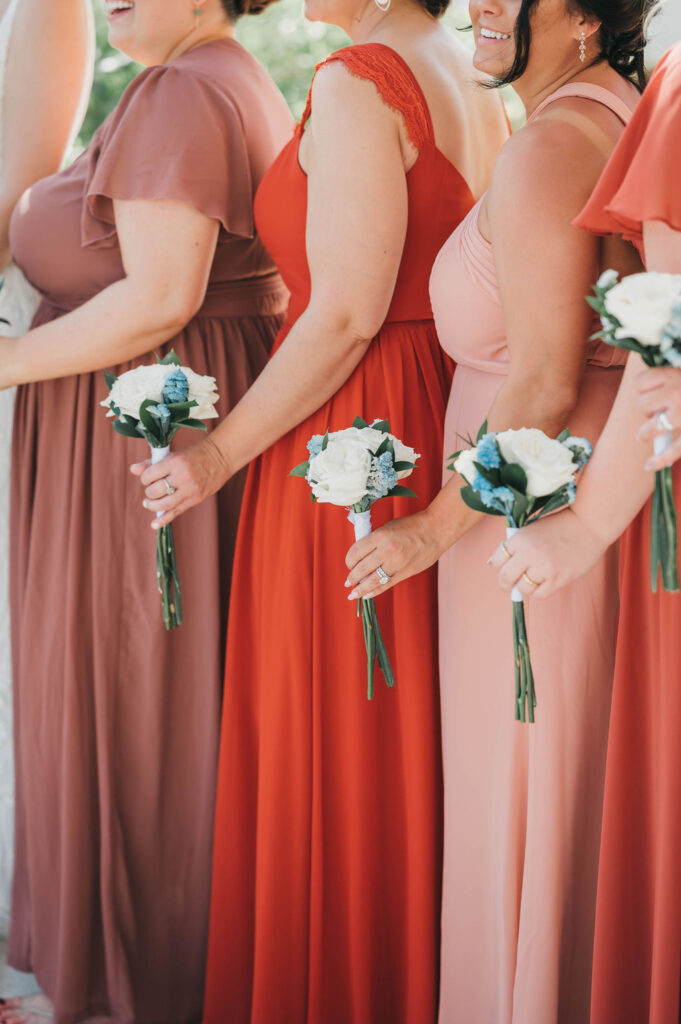 Four bridesmaids wearing dresses in shades of coral in mauve hold small nosegay bouquets