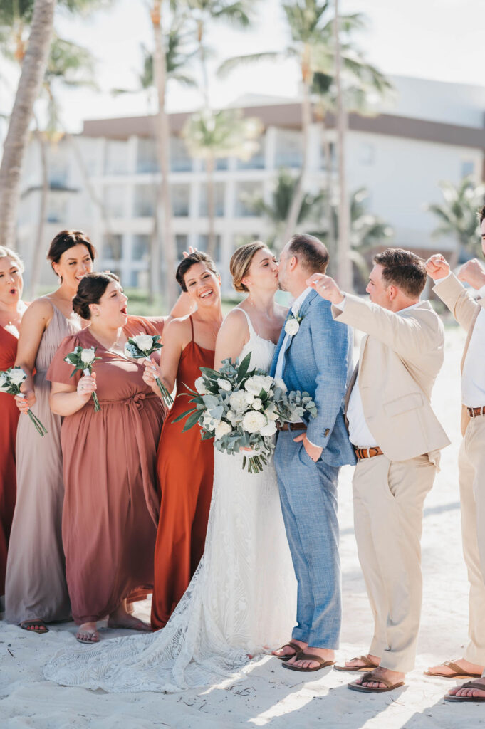 Bride and groom kiss while bridal party looks on and cheers