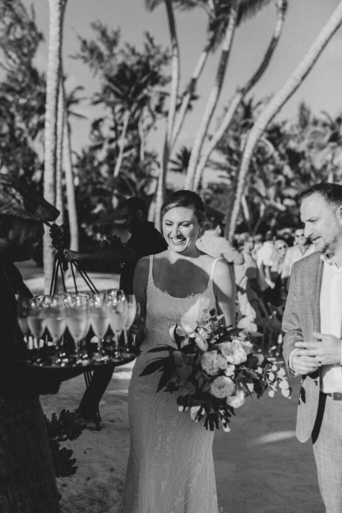 Black and white photo of a Hyatt Ziva staff member holding tray full of champagne while bride and groom look on