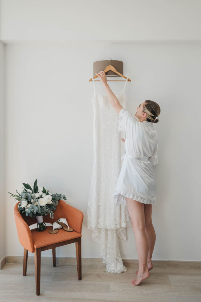 Bride reaching up to take wedding dress off hanger