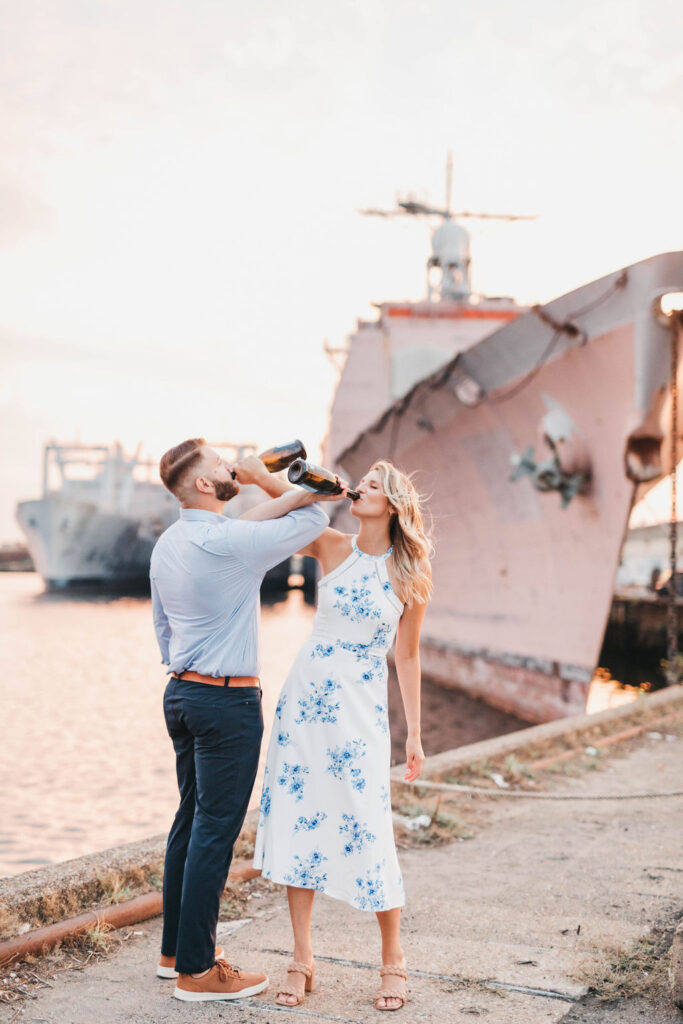Couple interlink arms while drinking from matching bottles of La Marca Prosecco at the Philadelphia Naval Yard at sunset