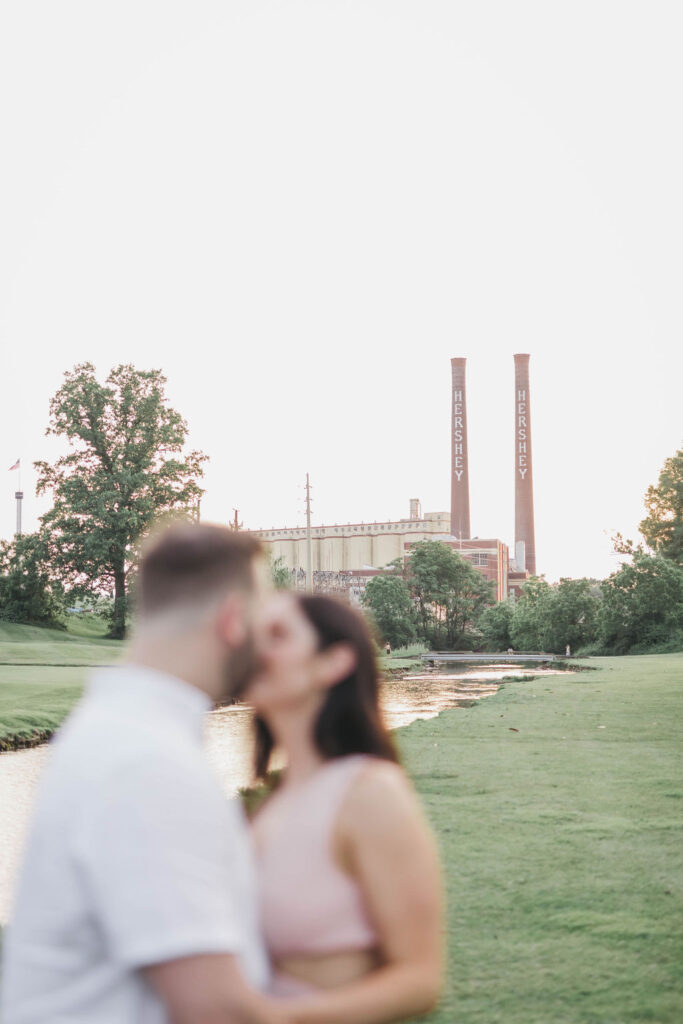 Couple kisses in front of 250' tall radial brick chimneys at the original Hersey Chocolate factory in Hersey, PA | Hershey Theater Engagement Photo Session by Lauren E. Bliss Photography