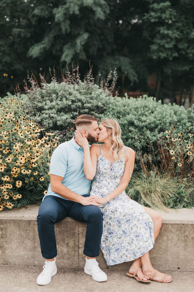 Couple kisses while sitting on a stone bench in front of a flower bed