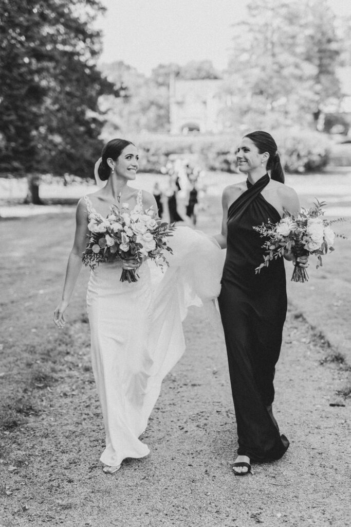 Bride and maid of honor looking at each other and smiling while walking outside during wedding photos
