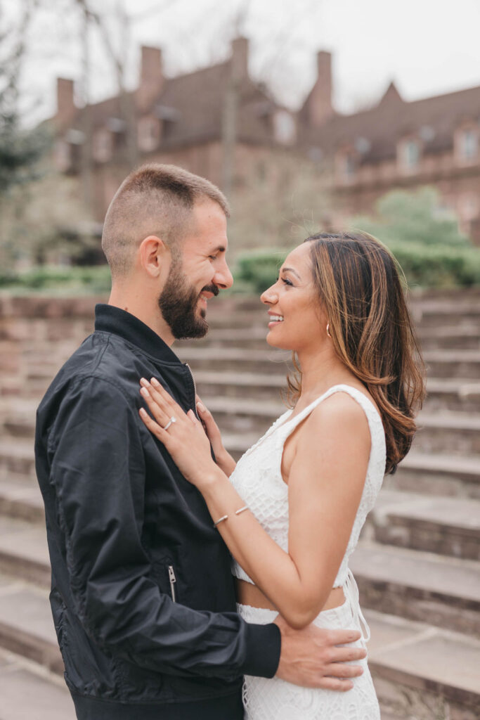 Man and woman face each other and smile in front of a brown stone staircase | Tyler Gardens Engagement Session Photos by Lauren E. Bliss Photography
