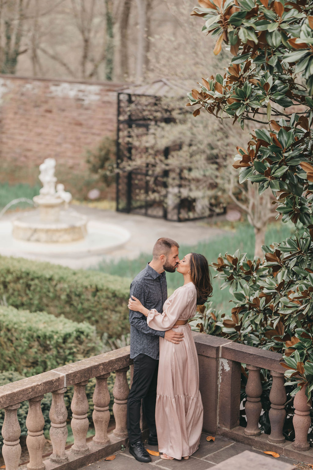 Man in woman kiss on carved stone staircase beside tall magnolia tree