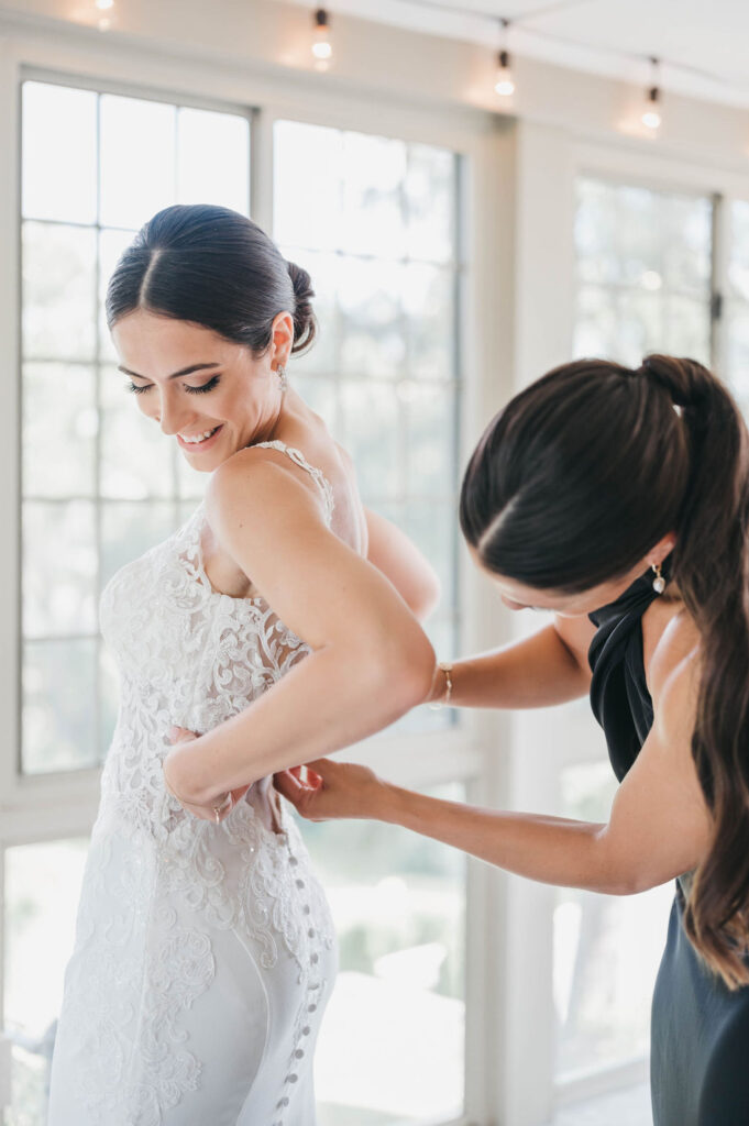 Maid of honor helping bride button the back of her wedding gown