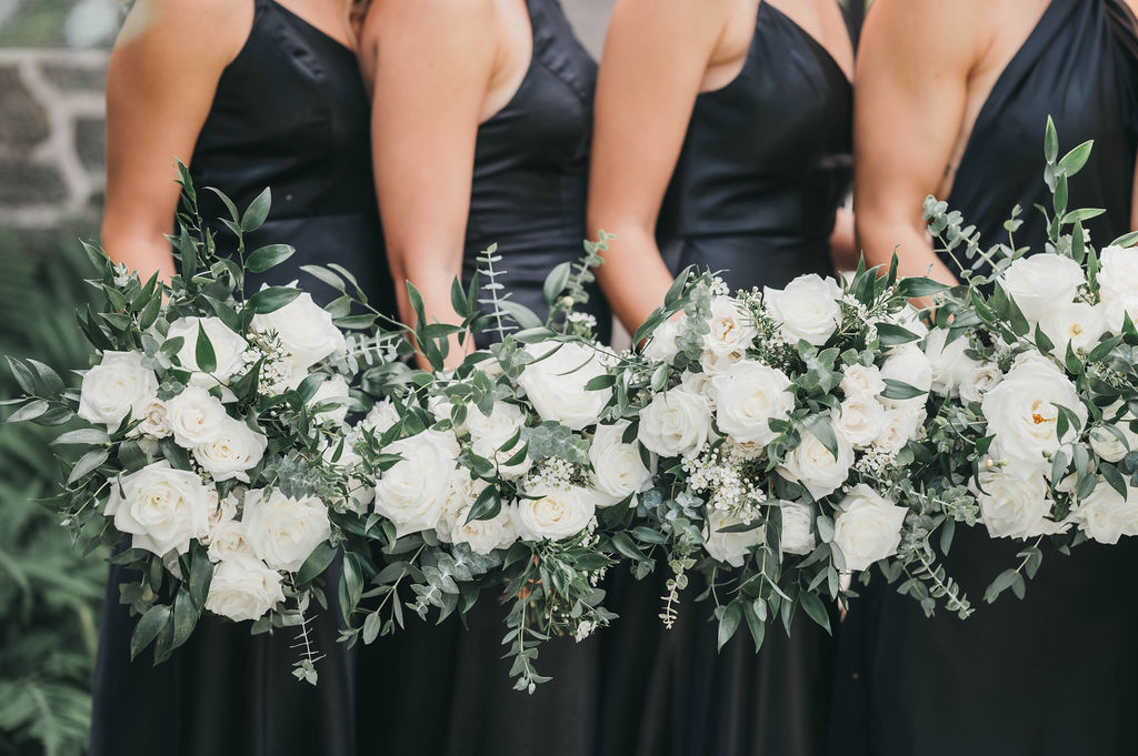 Close up of bridesmaids in black dresses holding floral bouquets of white and greenery