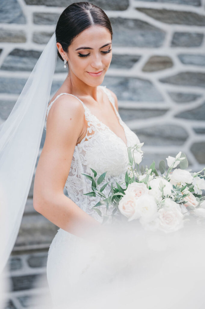 Bride holding white and green floral bouquet in front of stone wall at Greystone Hall venue in West Chester PA | Lauren E. Bliss Photography