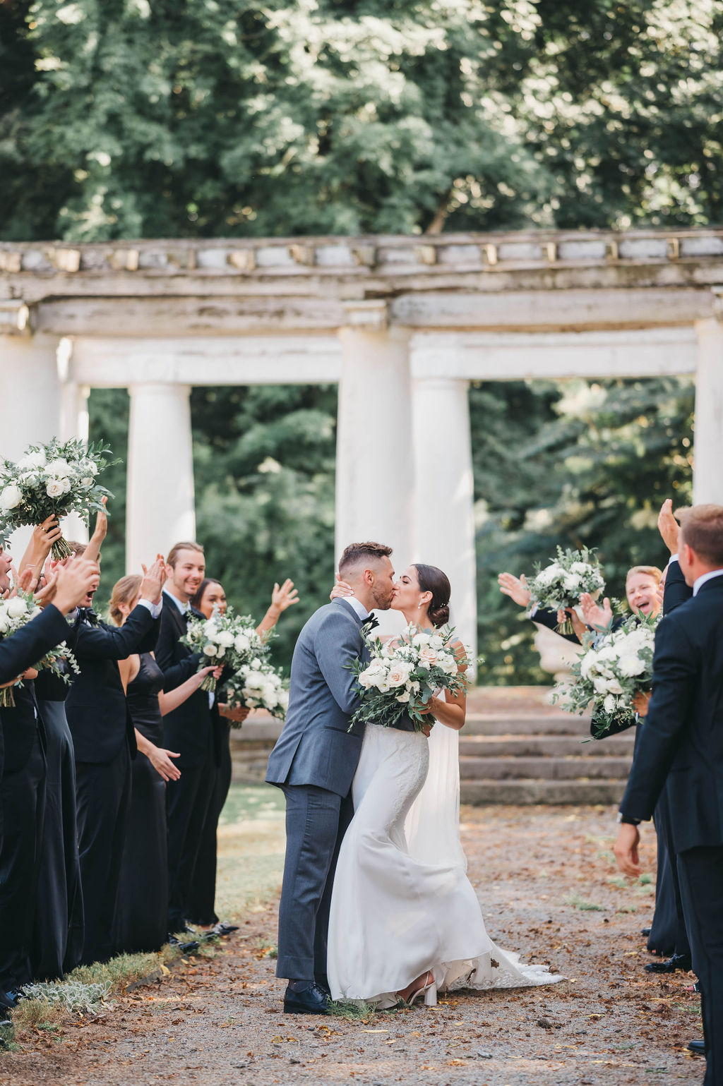 Bridal party in a black and white color palette surrounding bride and groom as they kiss under a pergola backdrop