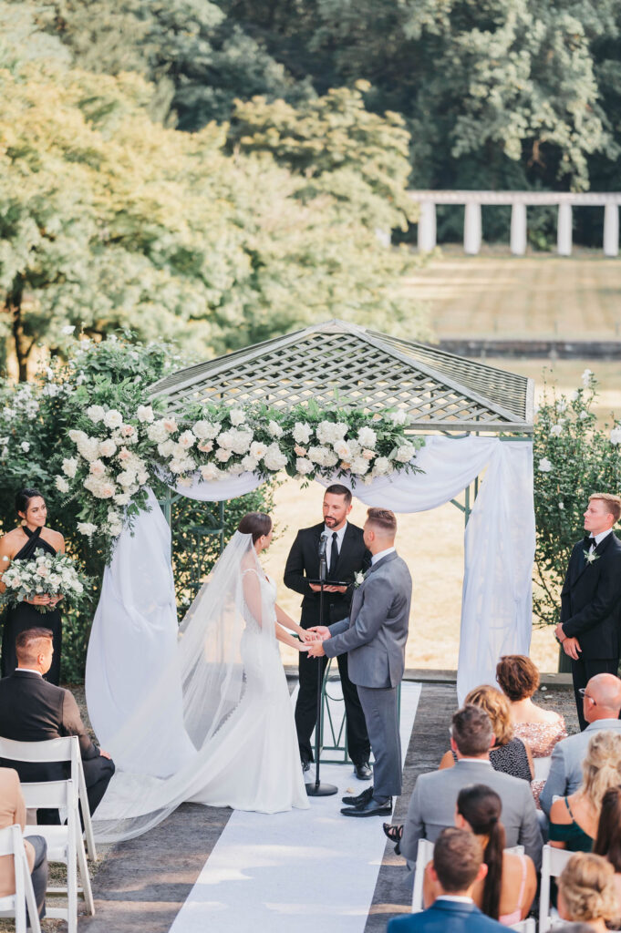 Bride and groom holding hands under a floral archway at their wedding ceremony at Greystone Hall in West Chester PA | | Lauren E. Bliss Photography Luxury PA Wedding Photographer