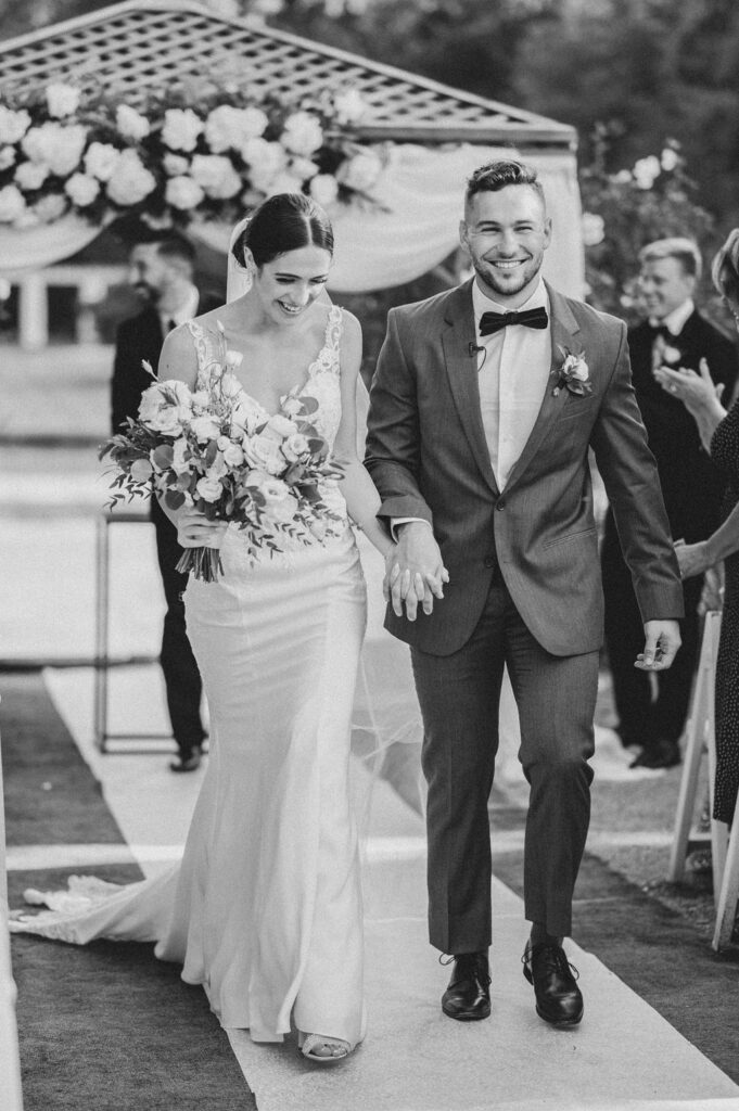 Black and white photo of bride and groom walking hand in hand down the aisle after their wedding ceremony