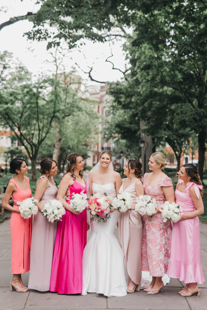 Bride poses in white mermaid style strapless dress with bridesmaids in six different pink mix and match dresses