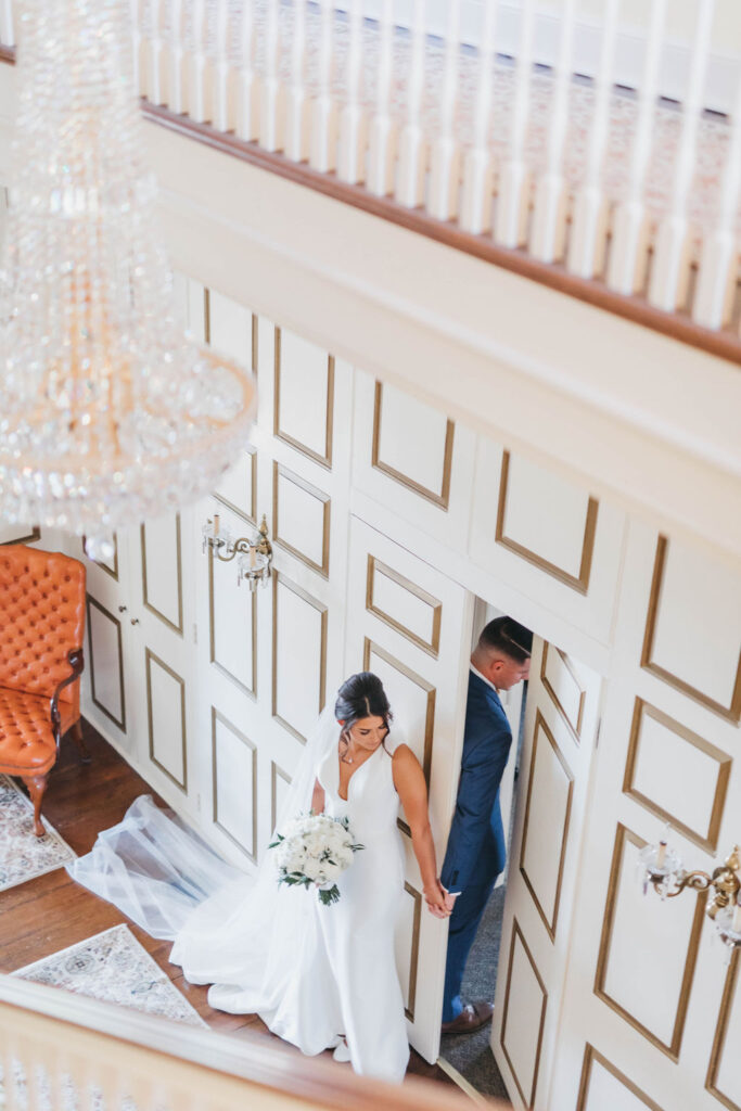Bride and groom hold hands through doorway during their first touch