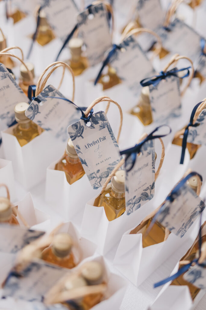 Small olive oil bottles in white paper bags tagged with a customized wedding favor note