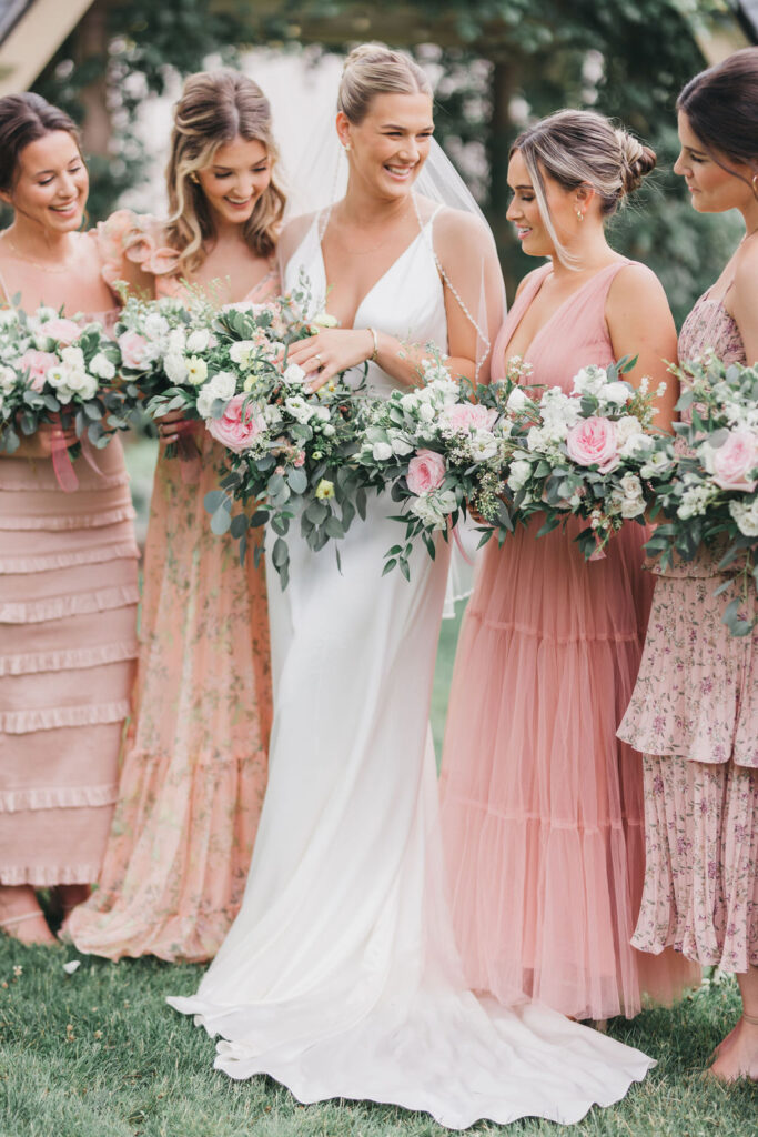 Bride stands in between 4 bridesmaids as they all hold cascading bouquets of eucalyptus and peonies