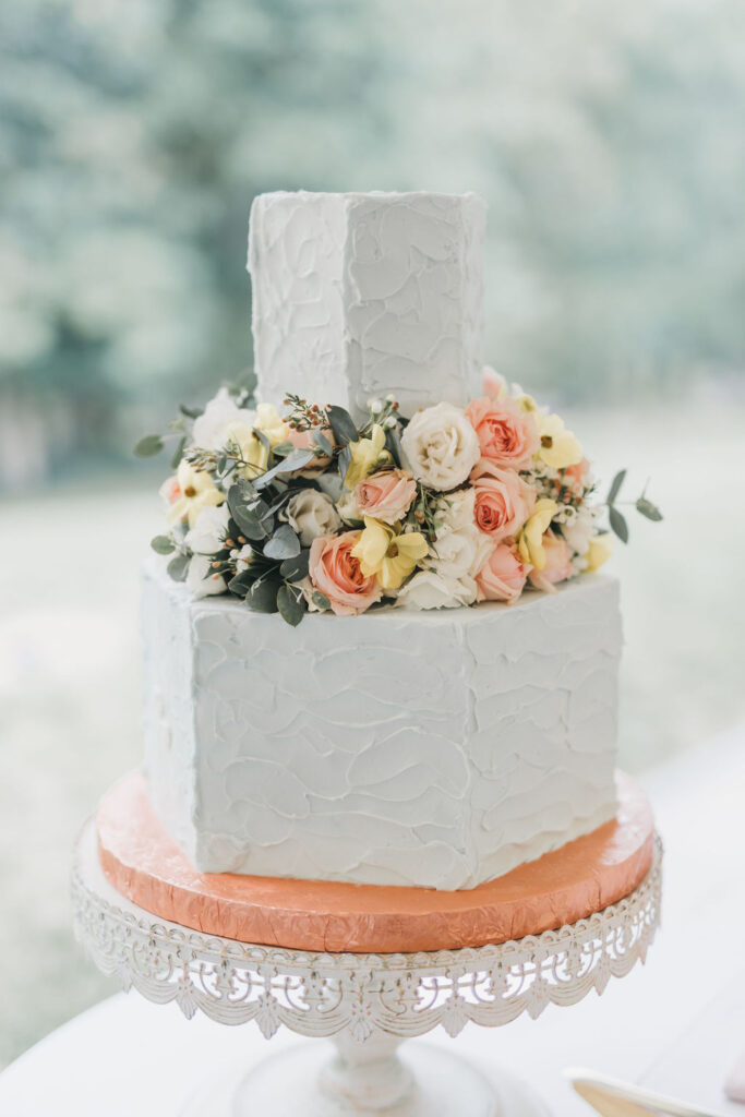 Two-tiered white wedding cake with middle tier made up of yellow and orange roses | Colorful wedding photography by Lauren E. Bliss Photography