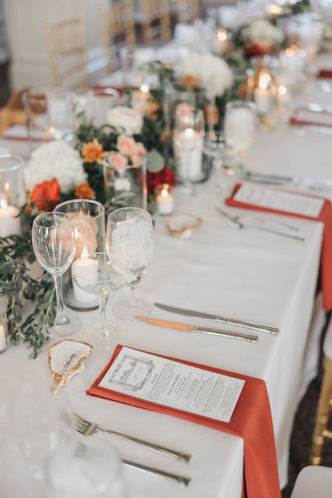 Banquet table covered in white tablecloth with rust colored napkins and floral centerpieces | Colorful wedding photography by Lauren E. Bliss Photography