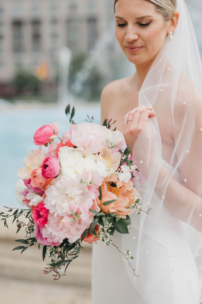 Bride looks down and smiles softly while holding round wedding bouquet of pink peonies