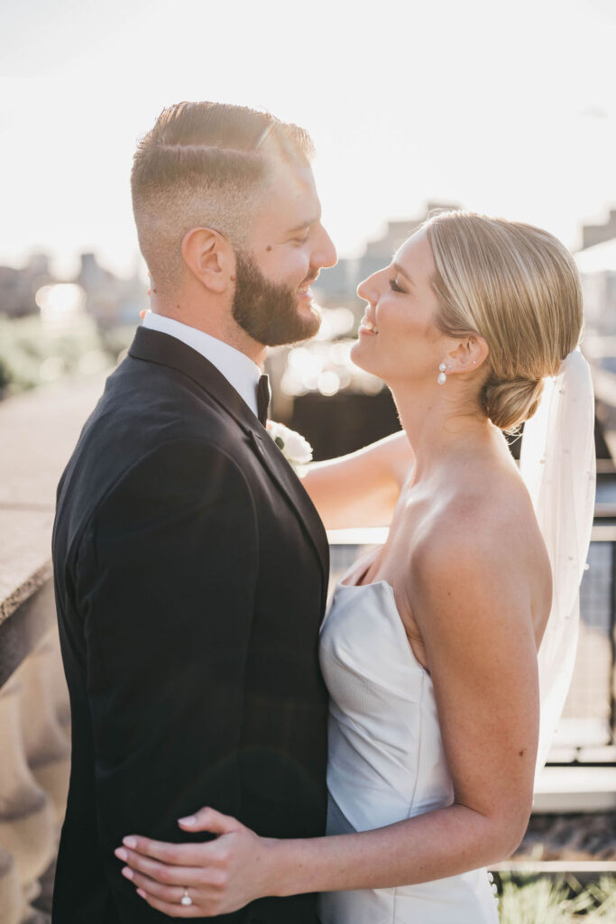 Bride and groom look at each other and smile during golden hour on the Free Library of Philadelphia rooftop