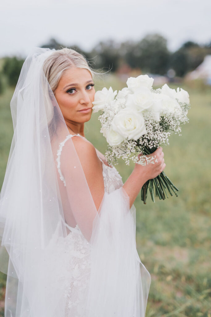 Bride looks over shoulder while holding up a bouquet of white roses and baby's breath