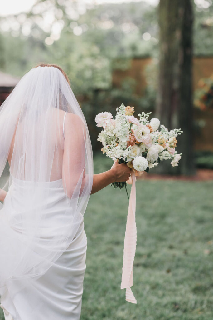 Bride walks away from camera while holding a hand tied bouquet of muted pastel fall flowers