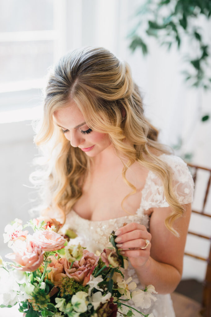 Bride looks down and smiles softly while holding a hand tied wedding bouquet of fall colors