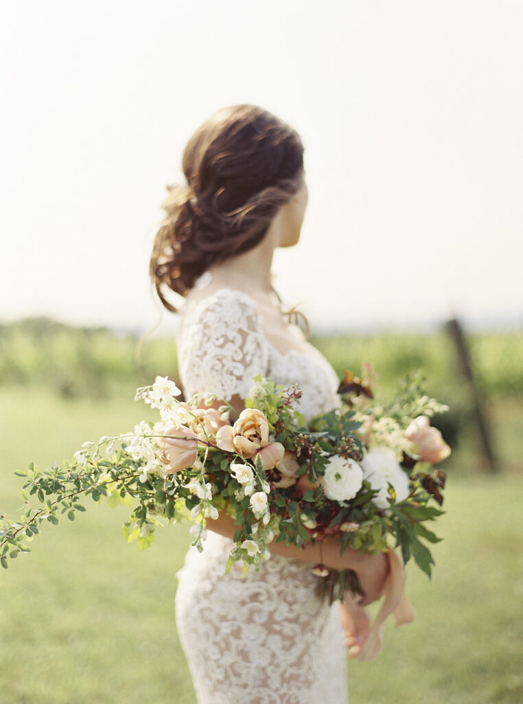 Bride in white lace dress cradles a fall colored pageant bouquet in the crook of her arm