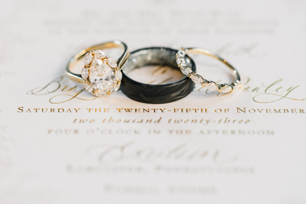 three rings sit on top of wedding invitation with gold script writing