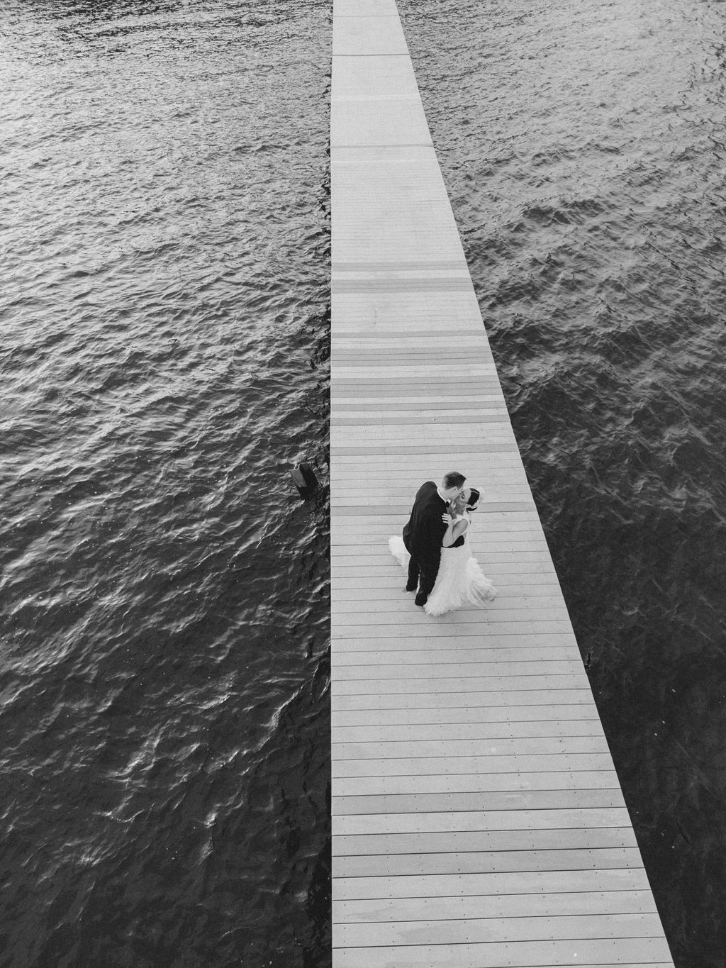 Black and white photo of a couple standing on a dock at the Mallard Island Yacht Club on their wedding day | Professional wedding photography by Lauren Bliss Photography