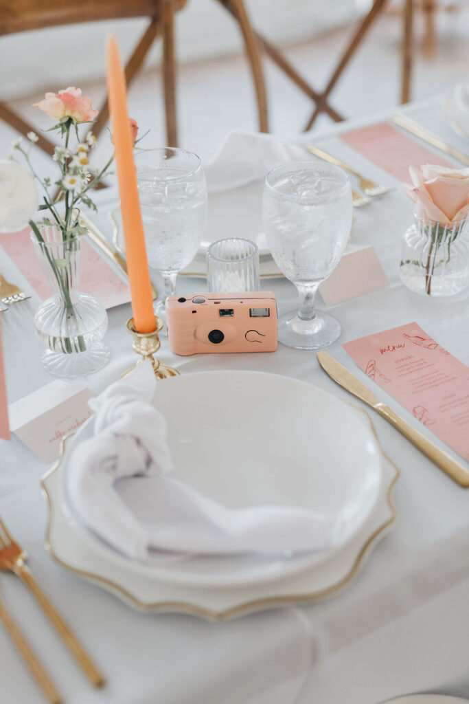 Peach colored wedding dinner menus sits on banquet table beside gold wedding flatware, white plates, and Pantone of the year 2024 wedding color palette