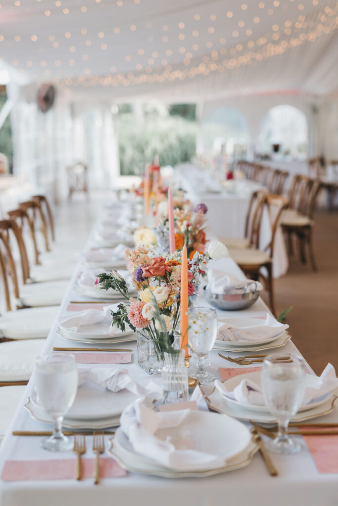 Banquet style wedding tablescapes decorated with a peach and pink color palette, gold flatware, and white linens