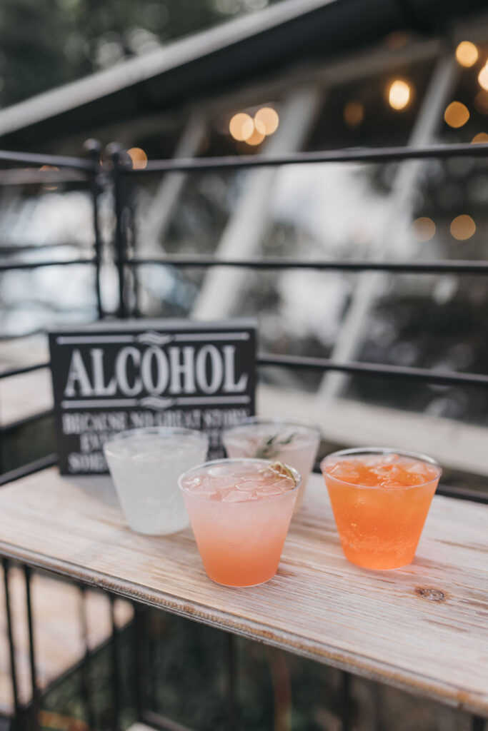 Four punch cups holding peach colored drinks sit on a wooden slab in front of a sign that says "Alcohol" | Lauren Bliss Wedding Photography in Philadelphia