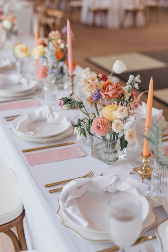 Banquet style wedding tablescapes decorated with a peach and pink color palette, gold flatware, and white linens