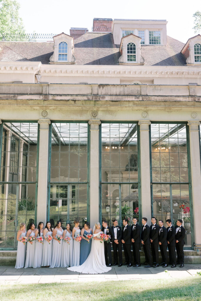 Bridal party wearing blue and black flanks a bride and groom on either side posing for wedding photos outside of Winterthur Museum and Gardens