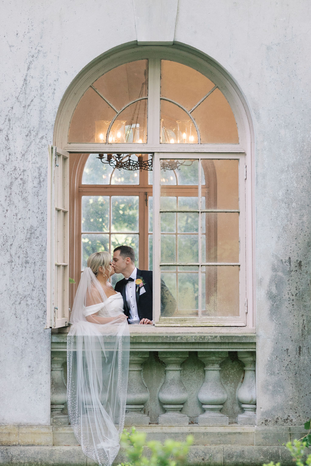 Bride and groom kiss behind an open arched window in a stone tower at Winterthur Museum and Gardens | Lauren Bliss Photography