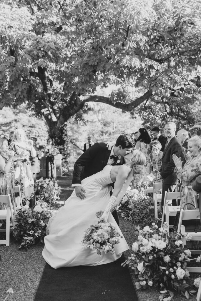 Groom dips bride into a kiss at the end of the wedding ceremony aisle | Lauren Bliss Photography at Elkins Estate in Philadelphia