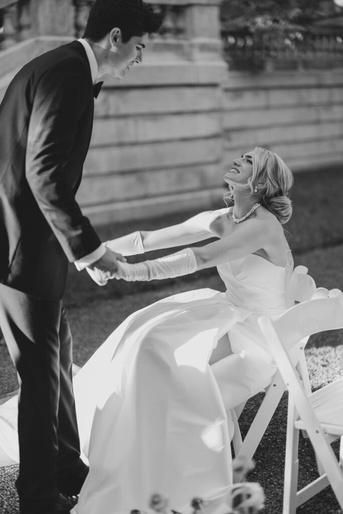 Groom stands over bride holding her hands as she sits in a chair | Lauren Bliss Photography at Elkins Estate in Philadelphia