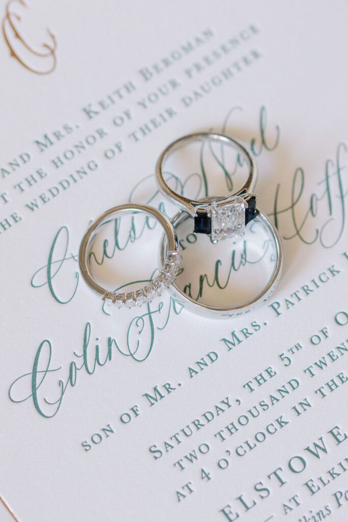 Three silver wedding rings lay on wedding invitation | Lauren Bliss Photography at Elkins Estate in Philadelphia