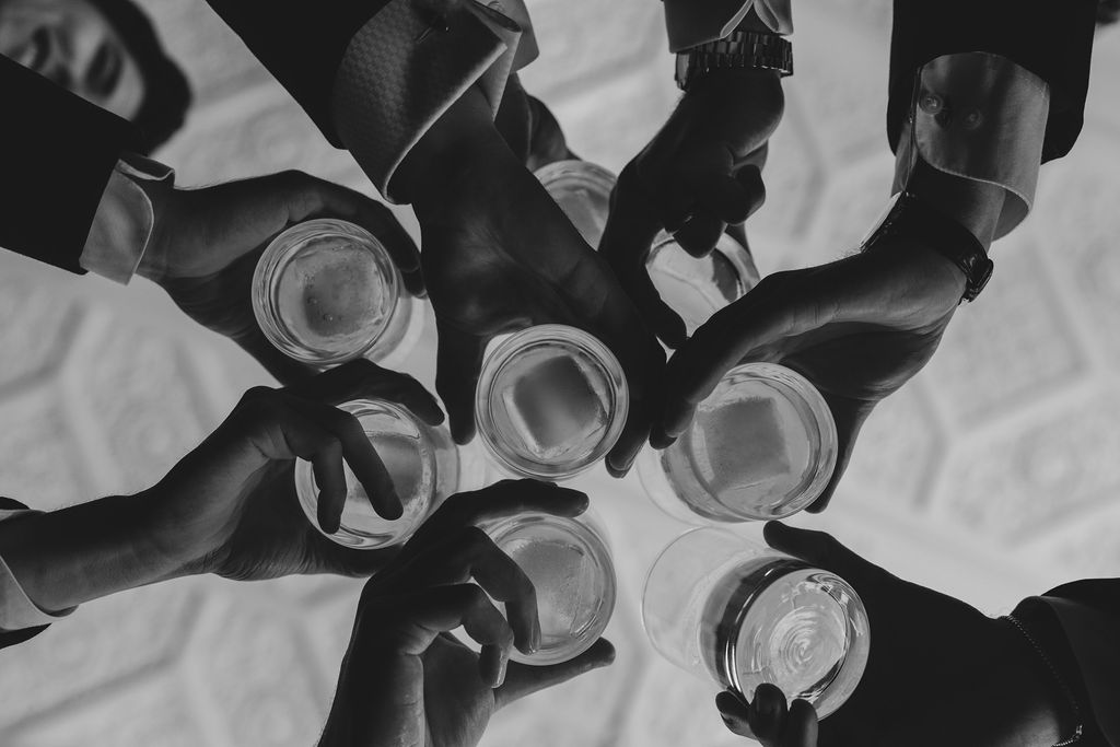 The underside of six whiskey glasses with square ice cubes clink in mid air above the camera | Lauren Bliss Photography at Elkins Estate in Philadelphia