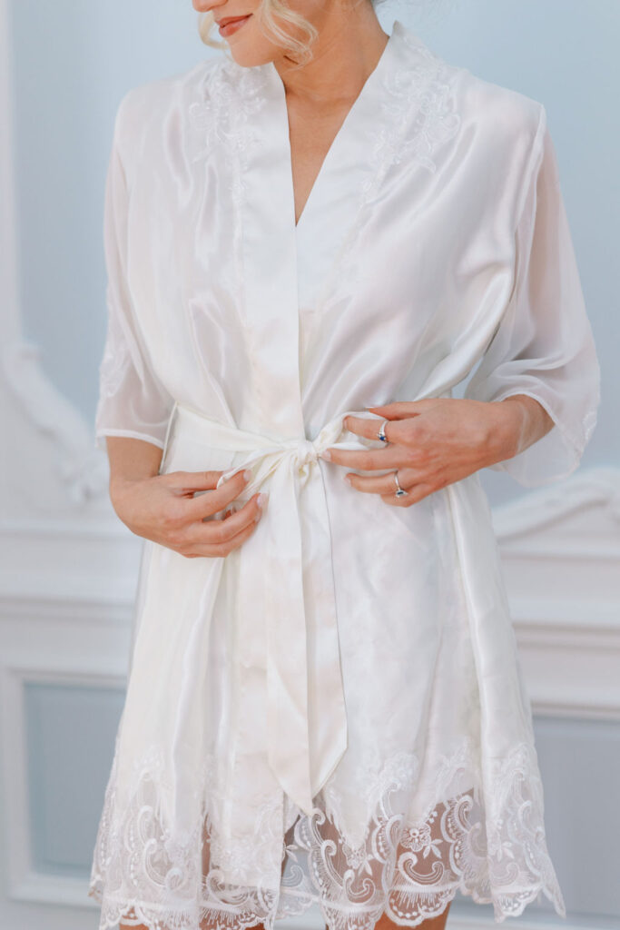 Bride ties a bow in her white silk robe | Lauren Bliss Photography at Elkins Estate in Philadelphia