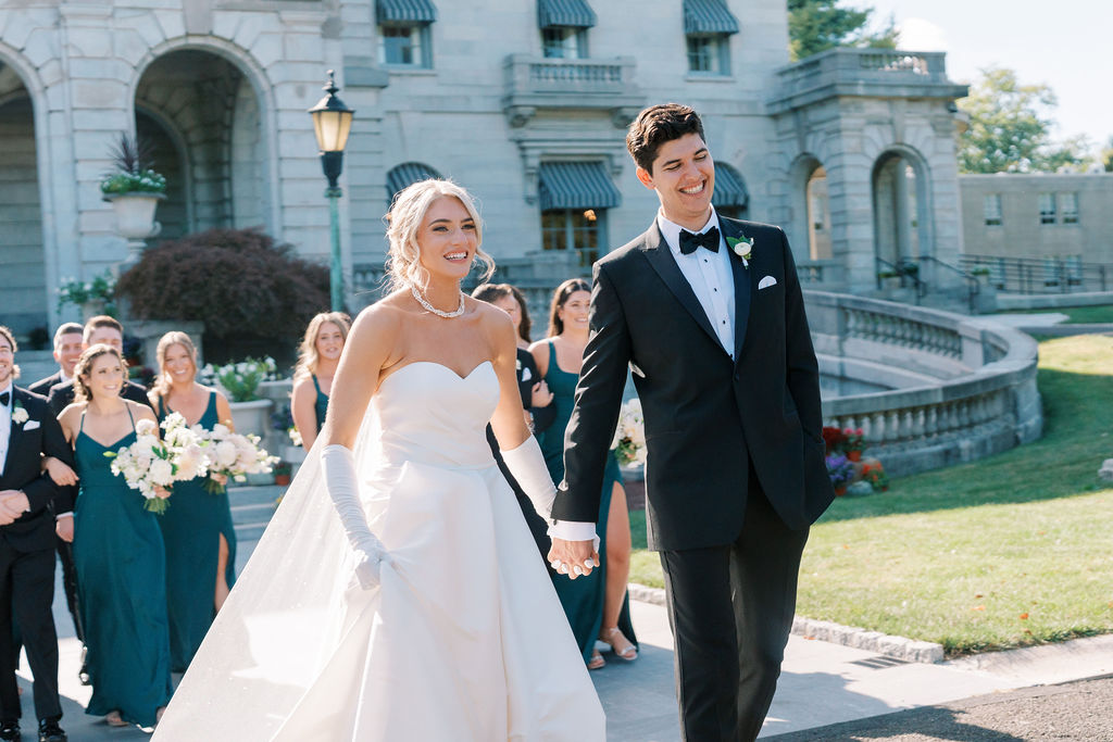 Bride and groom smile and hold hands while walking with their bridal party | Lauren Bliss Photography at Elkins Estate in Philadelphia