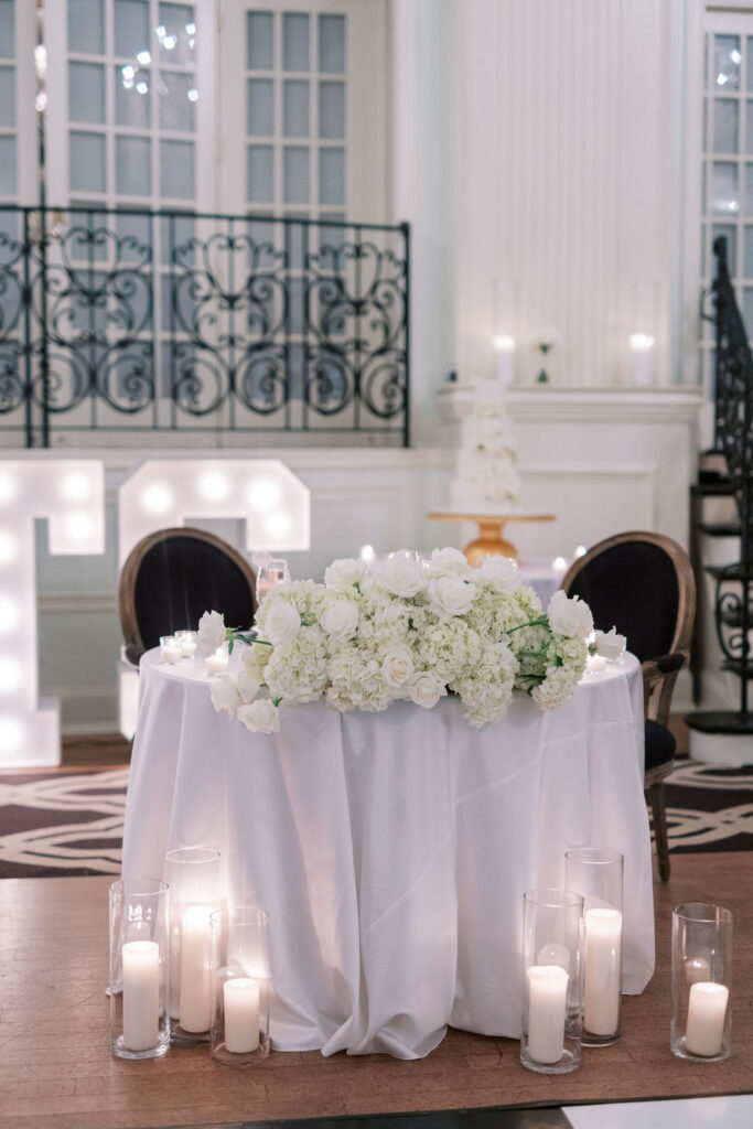 Sweeheart table with white linens and white florals sits in front of large light up sign | Wedding Photography by Lauren Bliss at the Cescaphe Ballroom Philadelphia