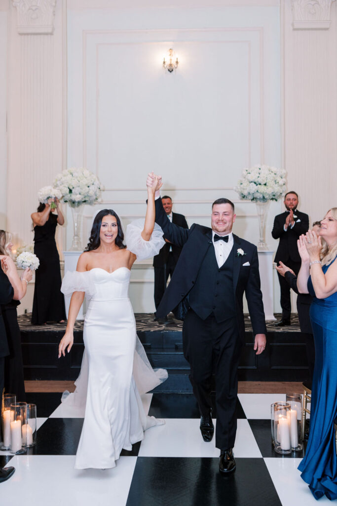 Bride and groom walk down wedding ceremony aisle holding raised hands | Wedding Photography by Lauren Bliss at the Cescaphe Ballroom Philadelphia