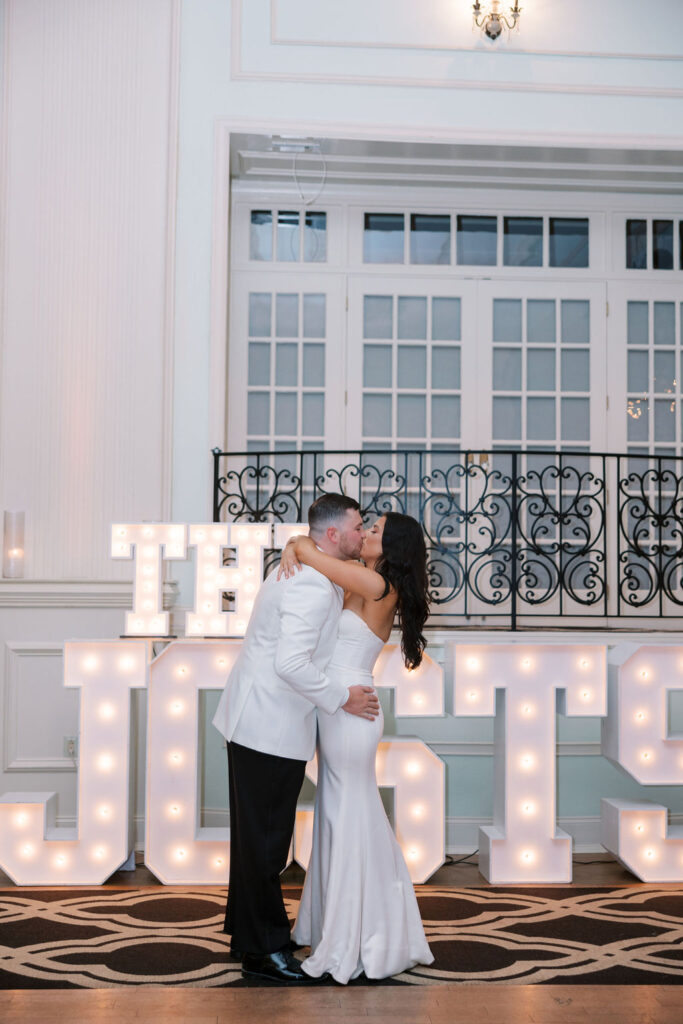 Bride and groom kiss in front of large light up sign that reads 'The Josts' | Wedding Photography by Lauren Bliss at the Cescaphe Ballroom Philadelphia