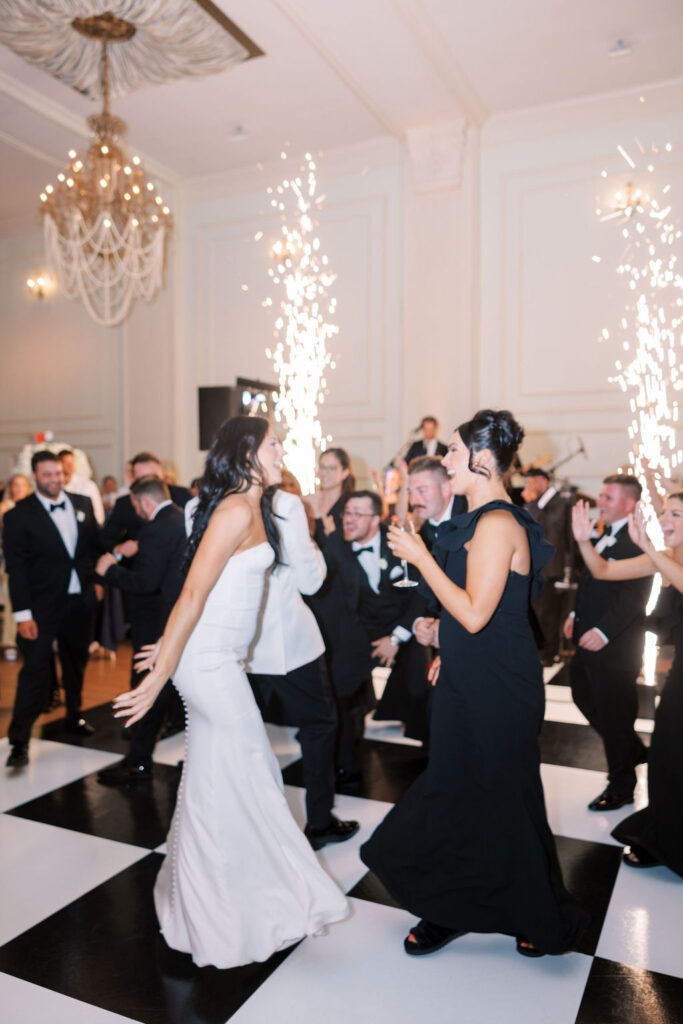 Bride and bridesmaid dance together on black and white checkered dance floor | Wedding Photography by Lauren Bliss at the Cescaphe Ballroom Philadelphia